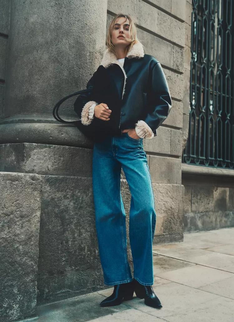 Model wearing black jacket and denim in an urban setting